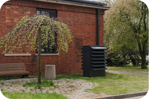 Nowoczesna obudowa akustyczna Silencions s|HP| na tle ceglanego budynku mieszkalnego, zapewniająca ciszę i estetyczny wygląd na osiedlu.