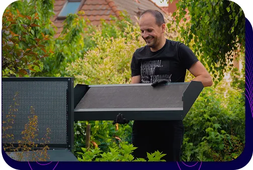 Uśmiechnięty mężczyzna, pracownik firmy Silencions, montujący obudowę na pompę ciepła w przydomowym ogrodzie.