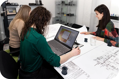 Zespół ekspertów Silencions - trzy osoby siedzące przy stole i analizujące plany techniczne oraz wyniki symulacji akustycznych na ekranie laptopa.