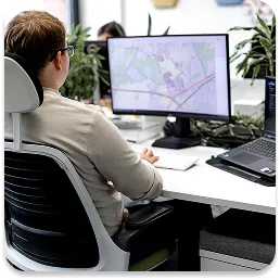 Osoba siedząca przy biurku, analizująca mapę na ekranie komputera. Obraz symbolizuje etap analizy wariantowej i optymalizacji, gdzie na podstawie danych opracowywane są różne scenariusze działań dla projektu.