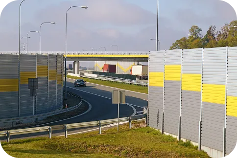 Zdjęcie autostrady, wzdłuż której ustawiono wysokie, kolorowe ekrany akustyczne. Obraz symbolizuje walkę z hałasem drogowym i modelowanie skuteczności ekranów w celu ochrony otoczenia przed nadmiernym dźwiękiem.