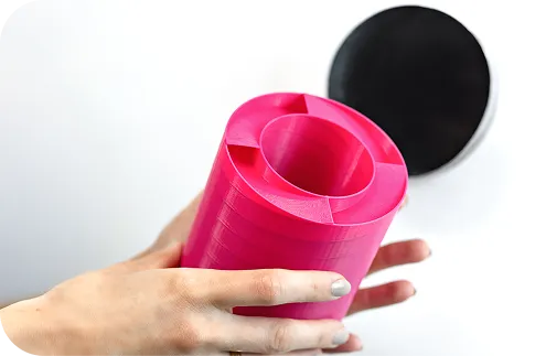 Zdjęcie przedstawiające różowy tłumik akustyczny s|TWIST trzymany w dłoniach, widoczny od góry. Widoczne są jego wewnętrzne przegrody i struktura, co podkreśla innowacyjną geometrię.