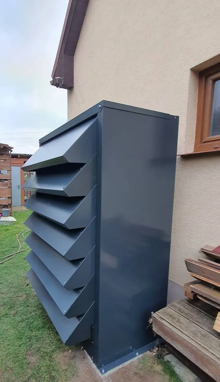 Wysoka, personalizowana obudowa na pompę ciepła w kolorze antracytowym zamontowana przy ścianie domu.