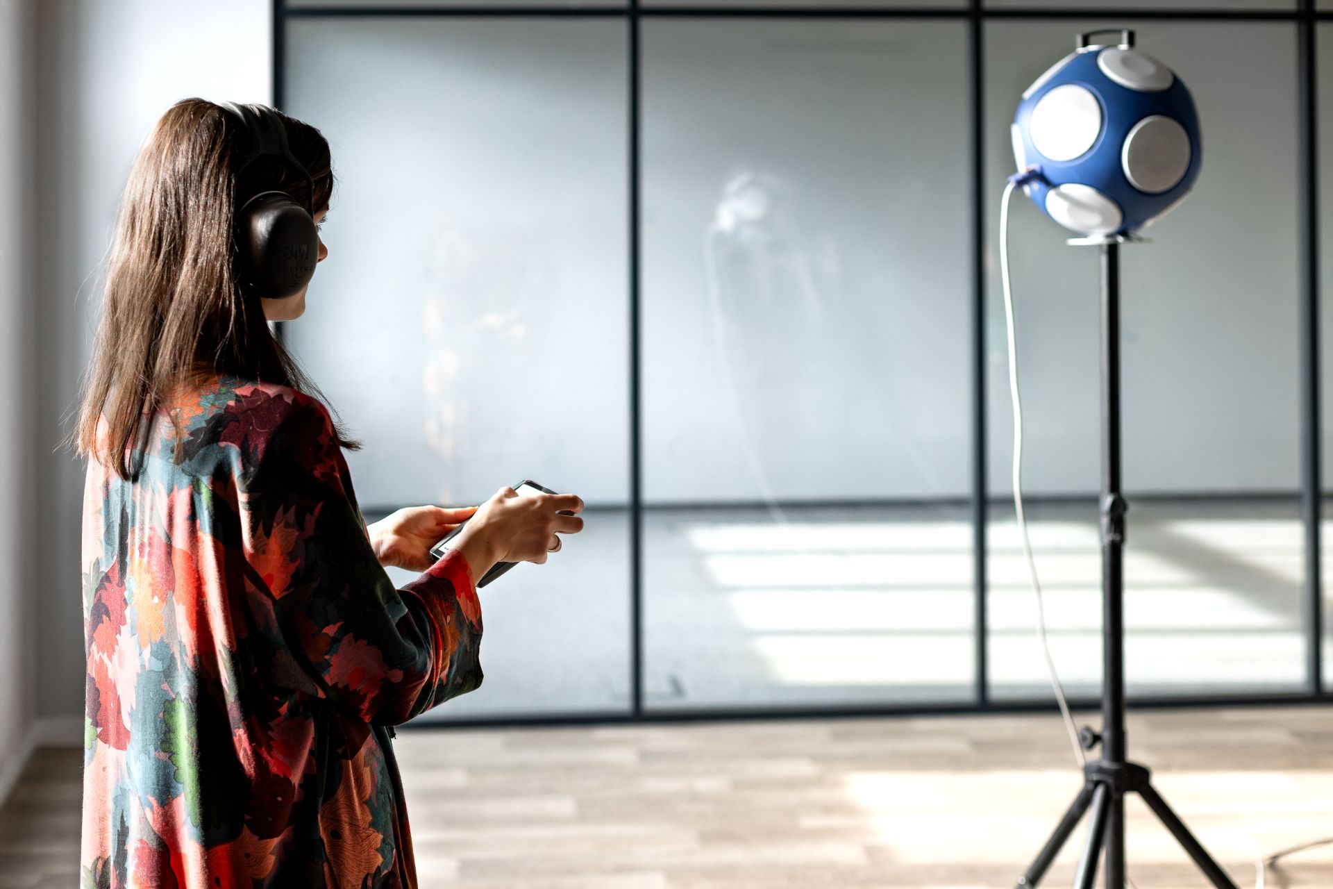 Inżynierka akustyki przygotowująca pomiar czasu pogłosu (RT60) w pomieszczeniu biurowym.