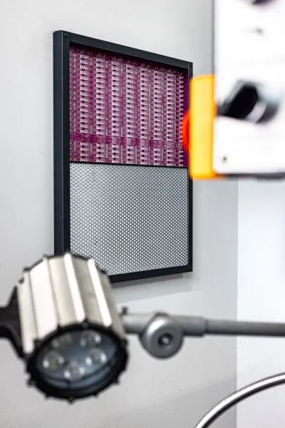 Zbliżenie na ścienny panel akustyczny s|MIX| Silencions, pokazujące różowy materiał pochłaniający dźwięk w górnej części oraz perforowaną blachę w dolnej części.