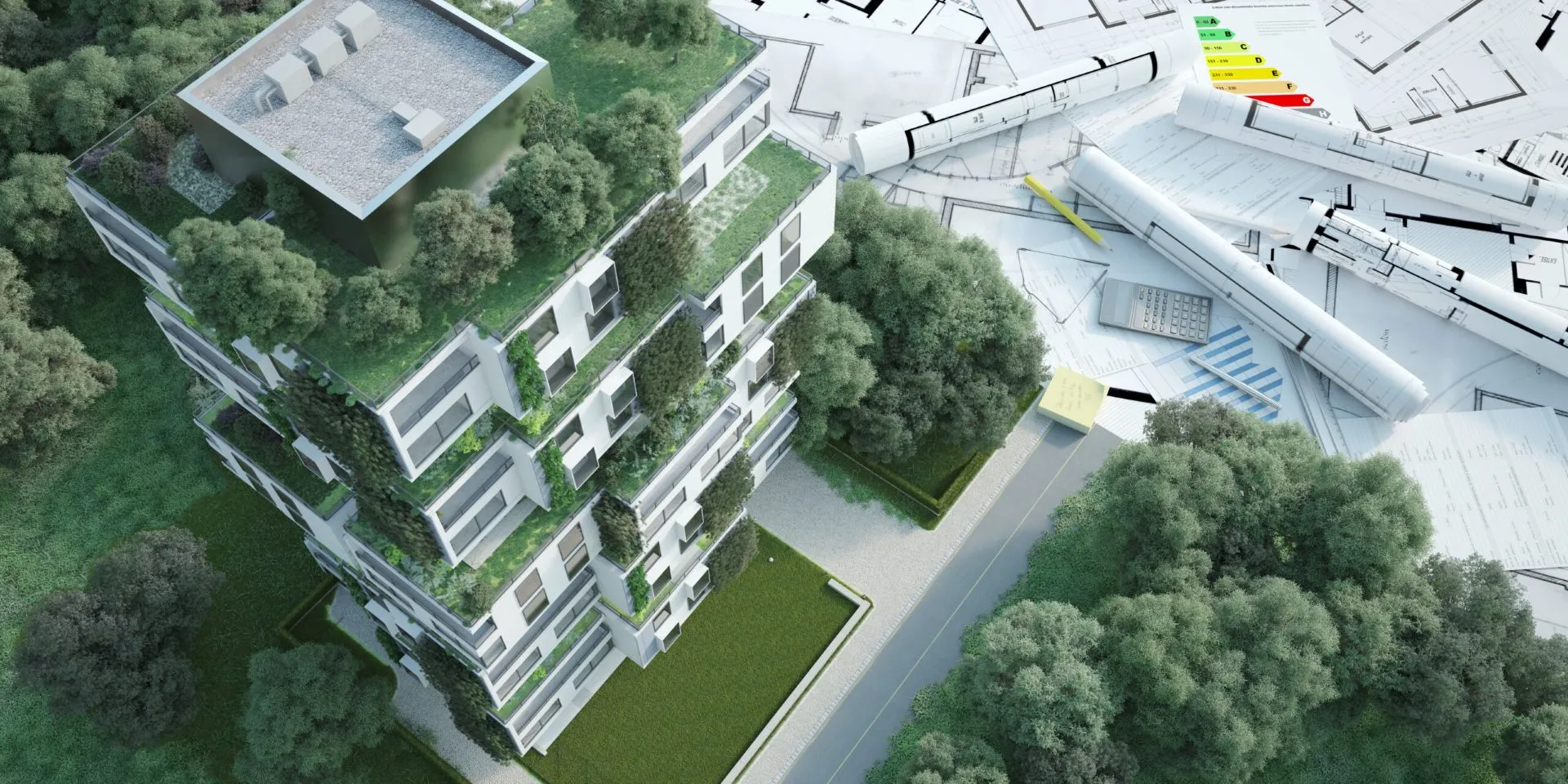 Wizualizacja nowoczesnego osiedla z zielonymi dachami i elewacją, widoczna z góry. Obok budynku leżą plany architektoniczne, rolka papieru, kalkulator i wykresy dotyczące efektywności energetycznej.